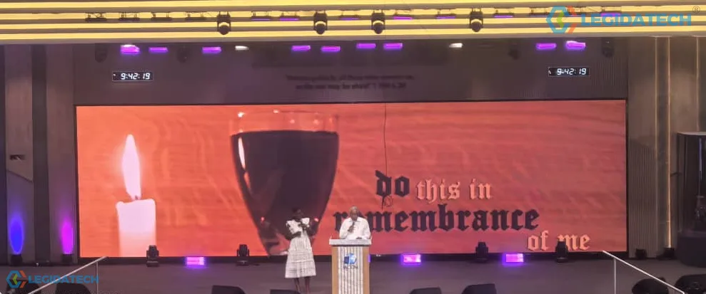 Communion service in a church auditorium - lyrics displayed across a large indoor LED wall